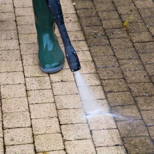 Skilled exterior cleaner restoring stained brick pavers with controlled surface washing equipment