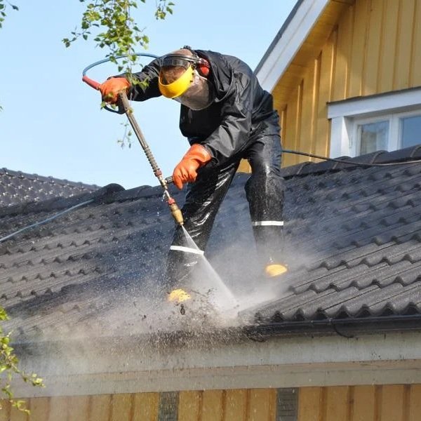 Technician brushing debris from gutter guards above a leaf-covered suburban roof edge